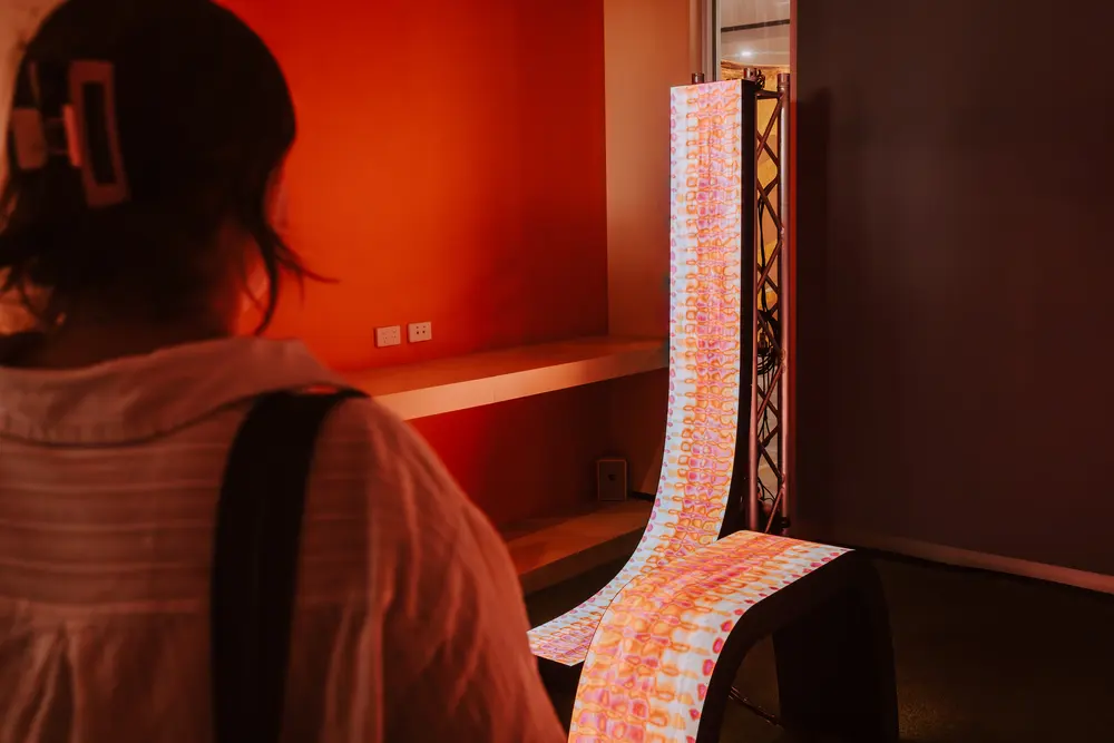 A visitor watches a patterned LED form curve down a red gallery wall