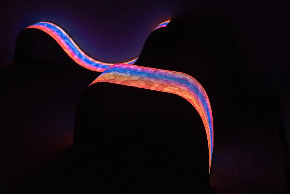 Undulating LED ribbon glowing red, blue and orange in a darkened gallery